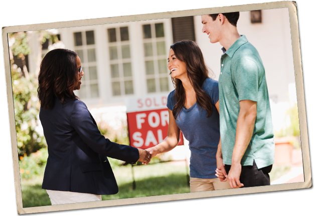A young couple shakes hands with a real estate agent in front of a For Sale sign.