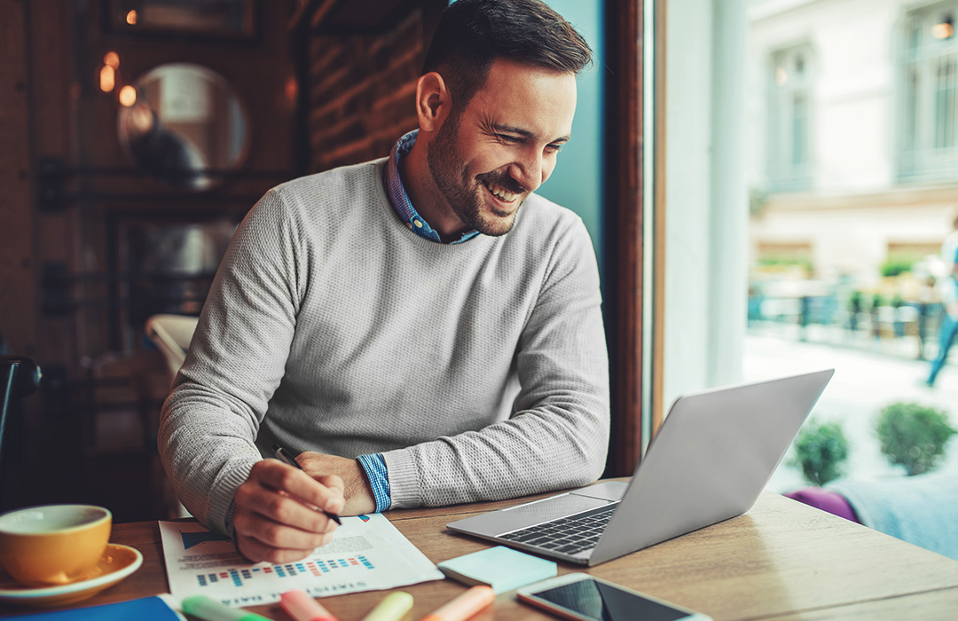 A man in a coffee shop works on a laptop